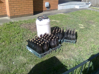 A brewing kit in a front yard with about 100 beer bottles neatly lined up around it