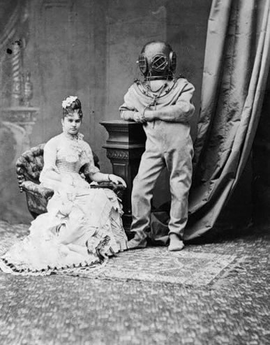Woman in C19th costume in ornate room with a man in old fashioned diving costume